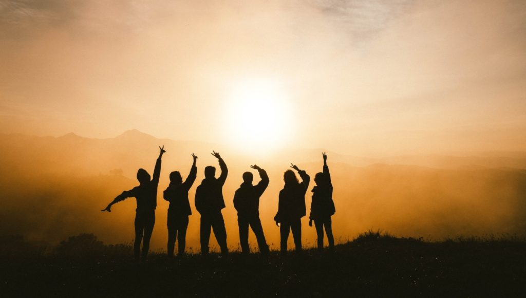 Gruppe von Menschen von hinten mit dem Sonnenuntergang hinter ihnen