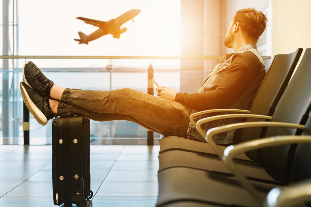 Mann, der auf einem Sitz am Flughafen sitzend ein abhebendes Flugzeug beobachtet