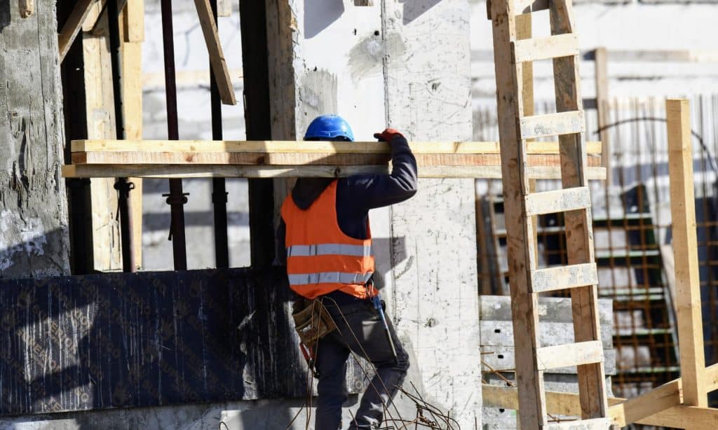 Mann trägt einen Balken über der Schulter und geht auf einer Baustelle in Australien.